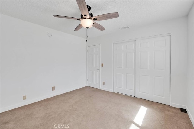 unfurnished bedroom with a textured ceiling, carpet floors, visible vents, baseboards, and a closet