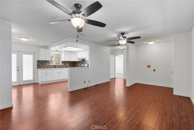 unfurnished living room featuring baseboards, a textured ceiling, visible vents, and dark wood-style flooring