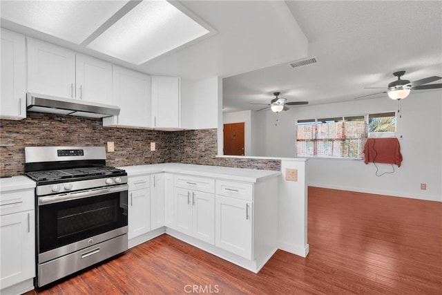 kitchen with a peninsula, backsplash, gas range, and under cabinet range hood