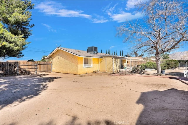 rear view of property featuring cooling unit, fence, and stucco siding