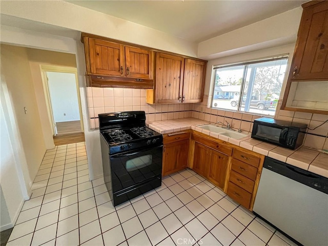 kitchen with tile countertops, decorative backsplash, a sink, under cabinet range hood, and black appliances