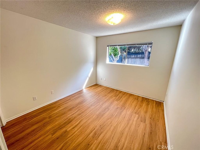 spare room featuring light wood-type flooring, baseboards, and a textured ceiling