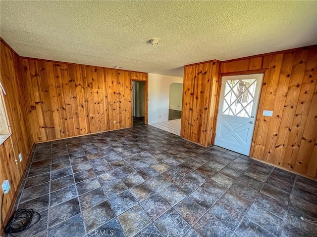 entrance foyer with wooden walls, arched walkways, and a textured ceiling