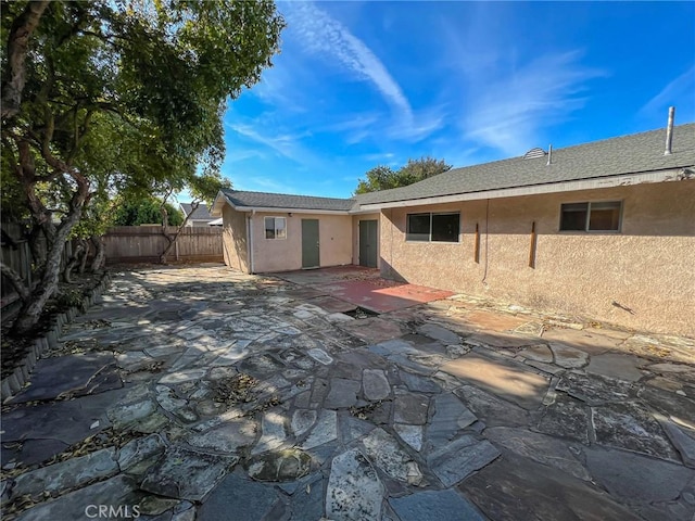 back of property with fence private yard, a patio area, roof with shingles, and stucco siding