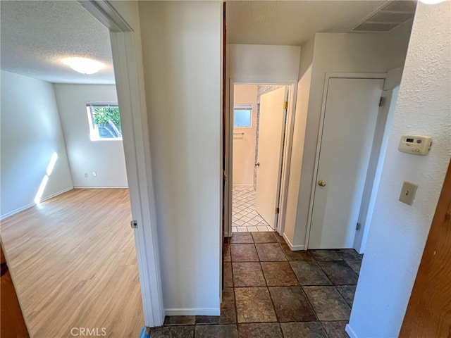 corridor featuring a textured ceiling, visible vents, and baseboards