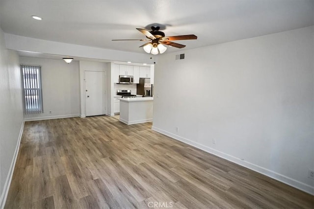 unfurnished living room featuring a ceiling fan, wood finished floors, visible vents, and baseboards