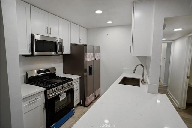 kitchen featuring white cabinets, light stone counters, stainless steel appliances, and a sink