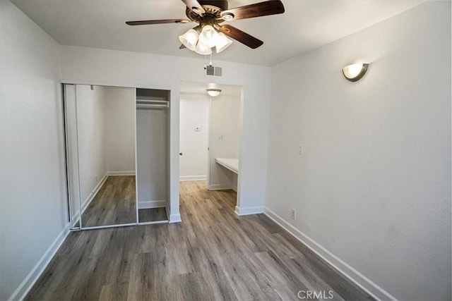 unfurnished bedroom featuring wood finished floors, a ceiling fan, visible vents, baseboards, and a closet