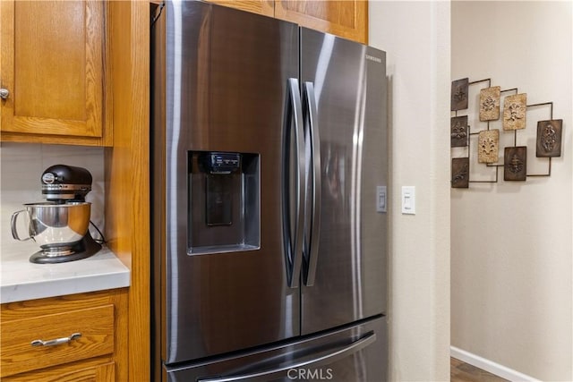 kitchen featuring light countertops, baseboards, brown cabinets, and stainless steel fridge with ice dispenser