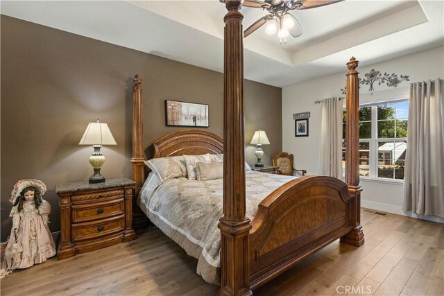 bedroom featuring a tray ceiling, visible vents, baseboards, and wood finished floors