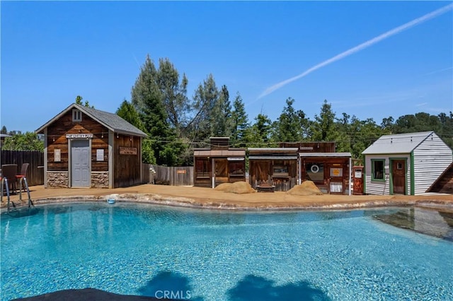 pool with an outbuilding, fence, a patio, and a storage structure