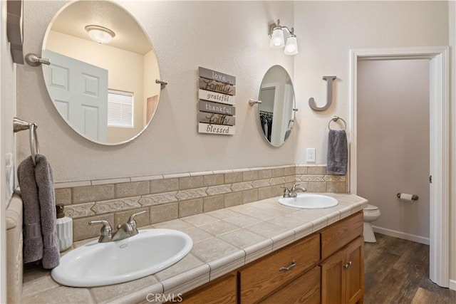 full bath with double vanity, a sink, toilet, and wood finished floors