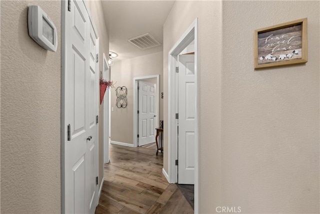 hallway with dark wood-style floors, baseboards, and visible vents