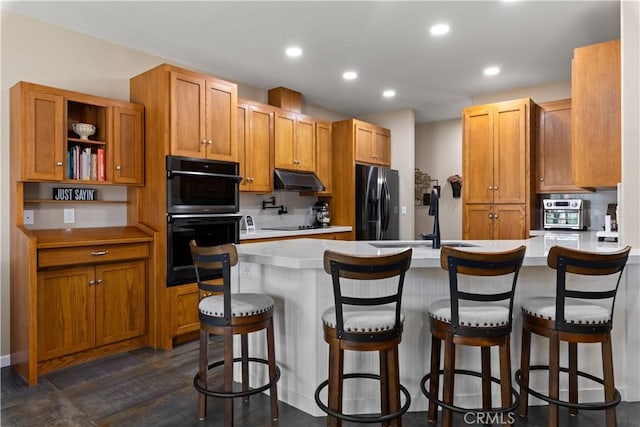 kitchen featuring light countertops, under cabinet range hood, black appliances, and a peninsula