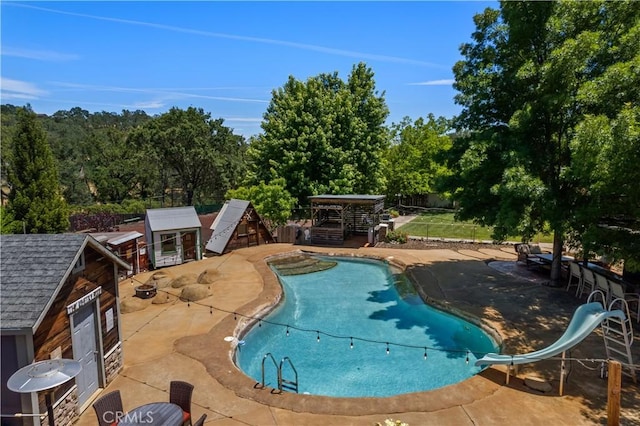 view of pool featuring an outbuilding, a water slide, fence, a fenced in pool, and a patio area