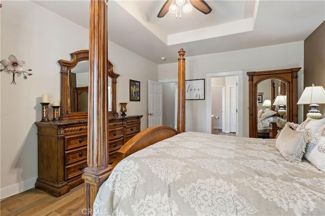 bedroom with a ceiling fan, a raised ceiling, light wood-style flooring, and baseboards