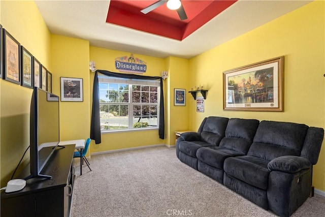 carpeted living room with a ceiling fan, a tray ceiling, and baseboards