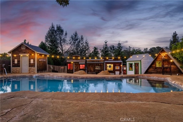 pool at dusk featuring a patio, an outdoor structure, an exterior structure, and fence