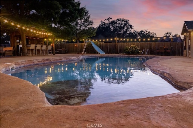 view of pool with a fenced in pool, a fenced backyard, outdoor dry bar, a water slide, and a patio area