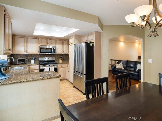 kitchen featuring arched walkways, light brown cabinets, stainless steel appliances, decorative backsplash, and a raised ceiling