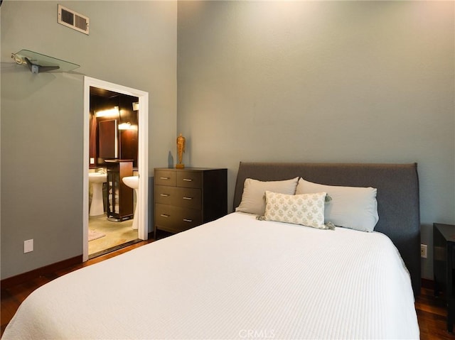 bedroom with ensuite bathroom, wood finished floors, visible vents, and baseboards