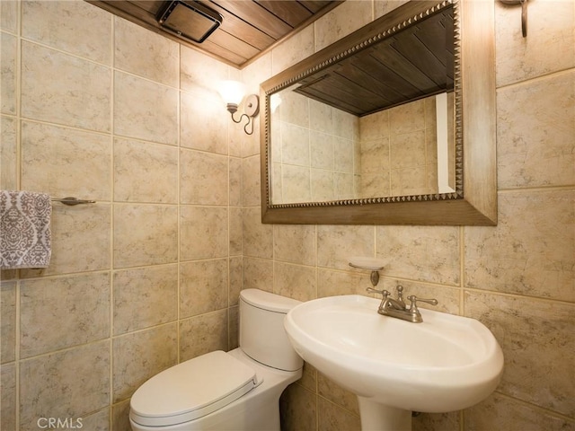 half bath featuring a sink, toilet, and tile walls