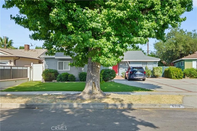 view of front facade featuring a front yard, concrete driveway, fence, and stucco siding