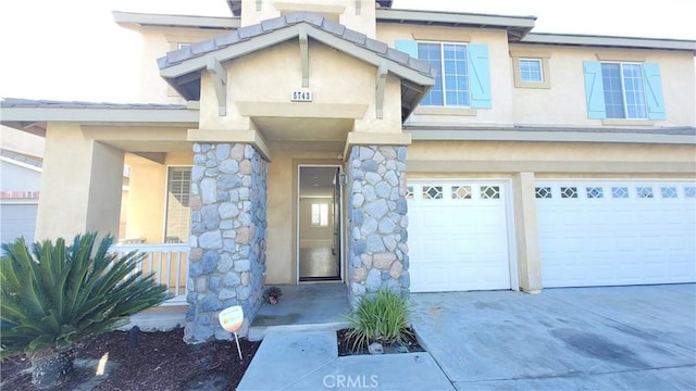 entrance to property with driveway, stone siding, an attached garage, and stucco siding