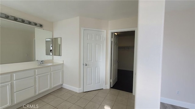 full bath featuring a walk in closet, vanity, baseboards, and tile patterned floors