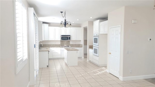 kitchen featuring pendant lighting, white double oven, stainless steel microwave, white cabinetry, and a sink