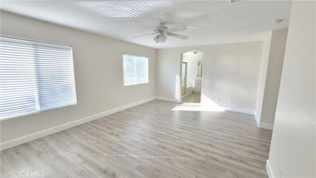 unfurnished room with arched walkways, ceiling fan, light wood-style flooring, and baseboards