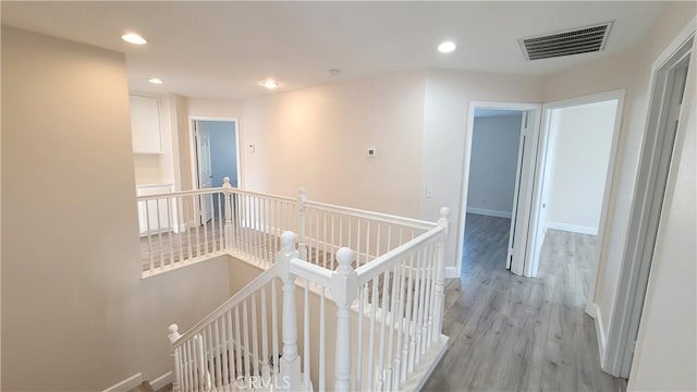 corridor featuring visible vents, light wood-style flooring, an upstairs landing, and recessed lighting