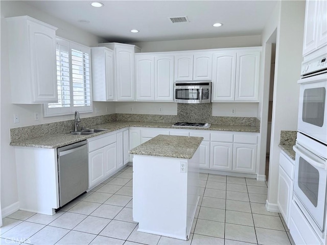 kitchen with light tile patterned floors, stainless steel appliances, a sink, and white cabinetry