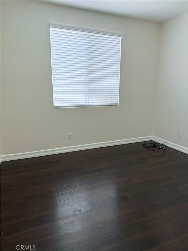 empty room with plenty of natural light, dark wood finished floors, and baseboards