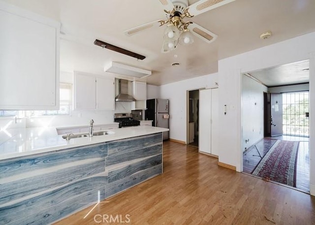 2116 Rancho Rd, El Sobrante, CA 94803 - kitchen featuring appliances with stainless steel finishes, wall chimney exhaust hood, light wood-style flooring, white cabinets, and a ceiling fan