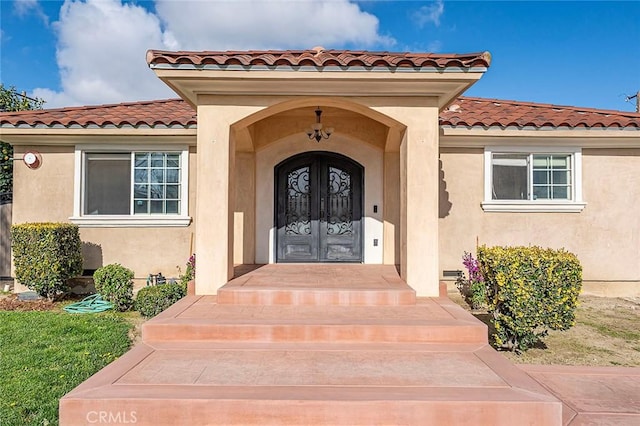 entrance to property featuring stucco siding, a tile roof, and french doors