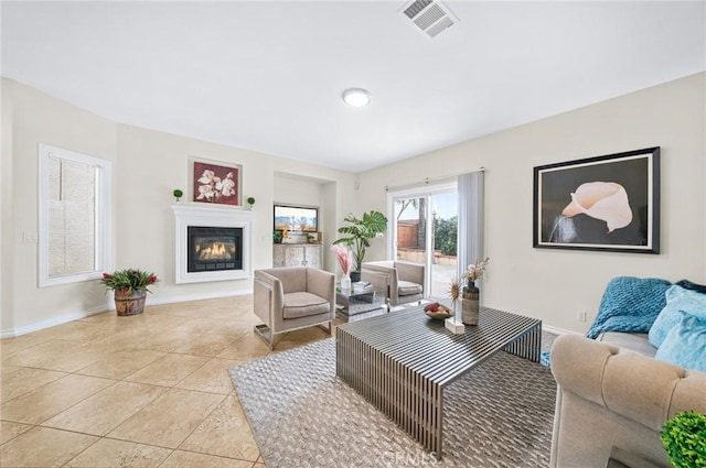 living area featuring light tile patterned floors, baseboards, visible vents, and a glass covered fireplace