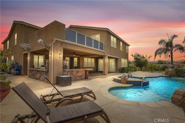 rear view of house with a pool with connected hot tub, a patio, outdoor dry bar, and stucco siding