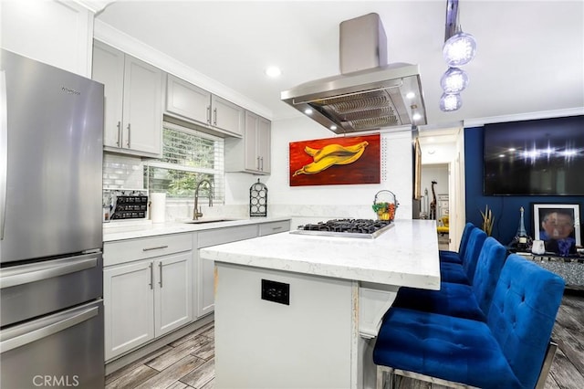 kitchen featuring light stone counters, wood finish floors, stainless steel appliances, a sink, and island range hood