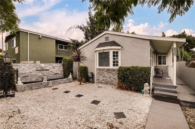 view of front of home with stone siding, fence, and stucco siding