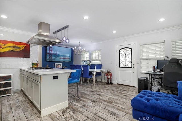 kitchen featuring a kitchen bar, stainless steel gas cooktop, island range hood, and ornamental molding