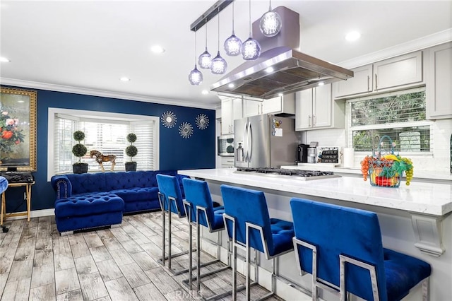 kitchen with light stone counters, island exhaust hood, stainless steel appliances, ornamental molding, and a kitchen breakfast bar