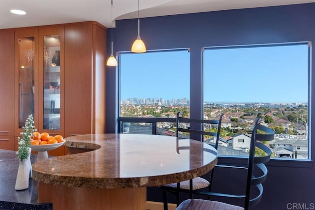 interior space with dark stone counters, glass insert cabinets, decorative light fixtures, a view of city, and recessed lighting