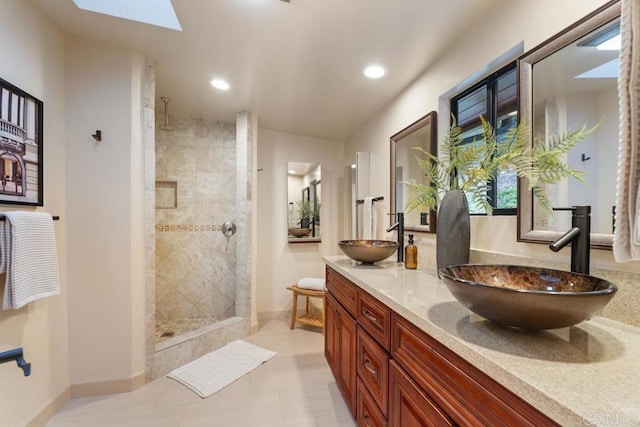 bathroom featuring a tile shower, a skylight, a sink, and baseboards