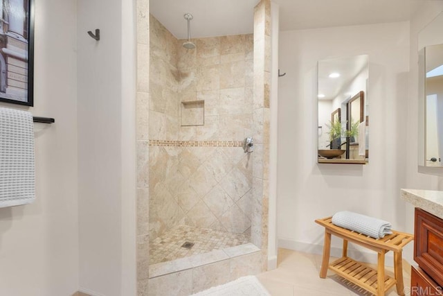 bathroom featuring tile patterned flooring, tiled shower, vanity, and baseboards