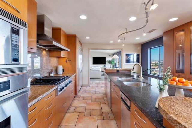 kitchen featuring wall chimney exhaust hood, appliances with stainless steel finishes, brown cabinetry, and a sink