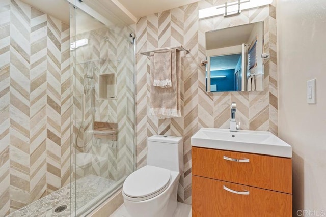 full bathroom featuring a stall shower, tile walls, toilet, vanity, and backsplash