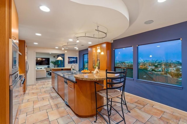 kitchen featuring brown cabinets, dark stone countertops, stainless steel appliances, a kitchen bar, and a sink