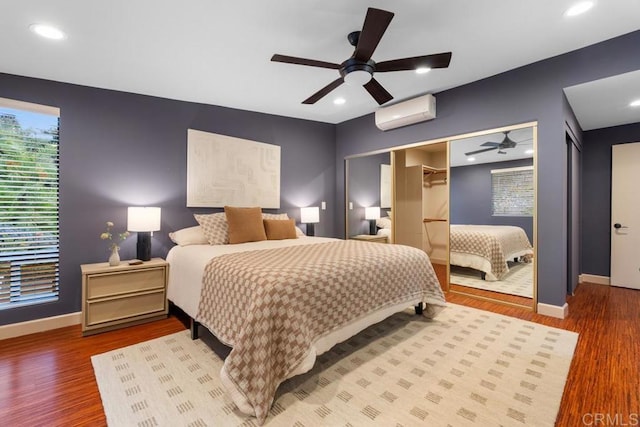 bedroom featuring ceiling fan, a wall mounted AC, baseboards, and wood finished floors