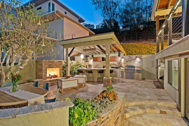 view of patio / terrace featuring an outdoor stone fireplace, a grill, and an outdoor kitchen